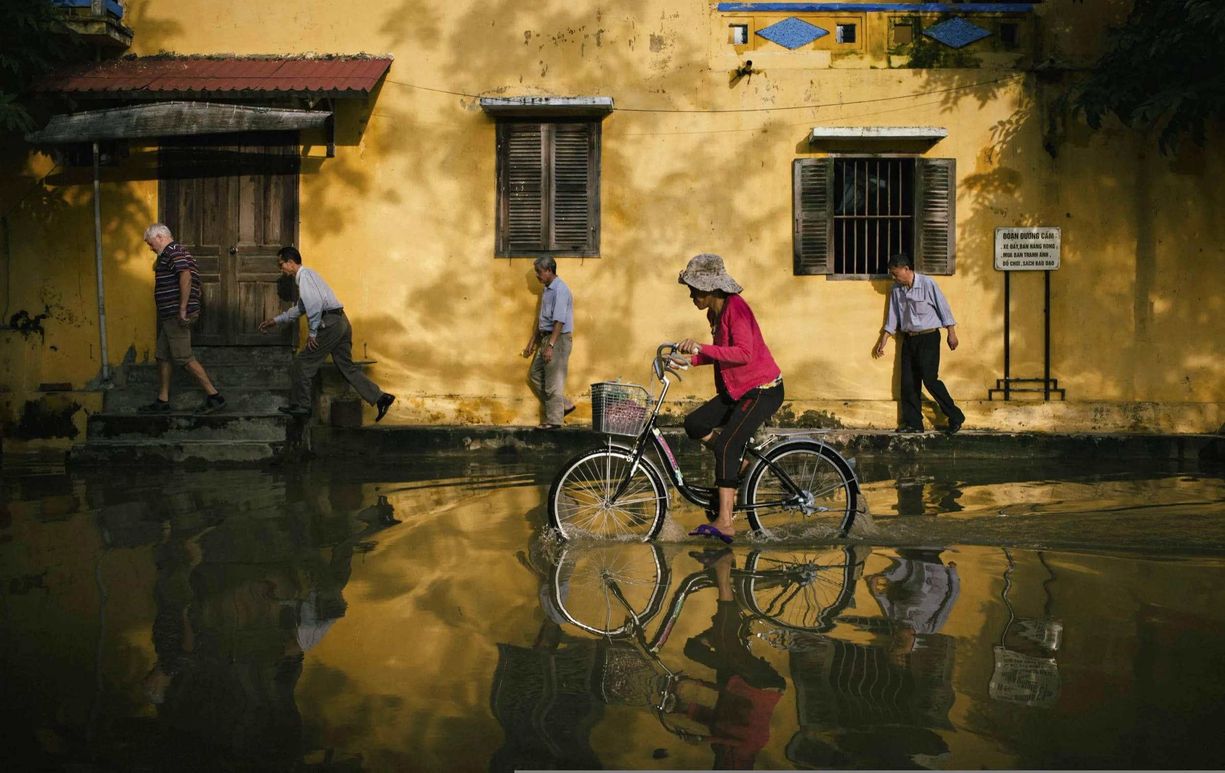 Daily life in Hoi An Old Town: a cyclist rides through a flooded street past mustard-yellow heritage walls on a Fingo private tour.
