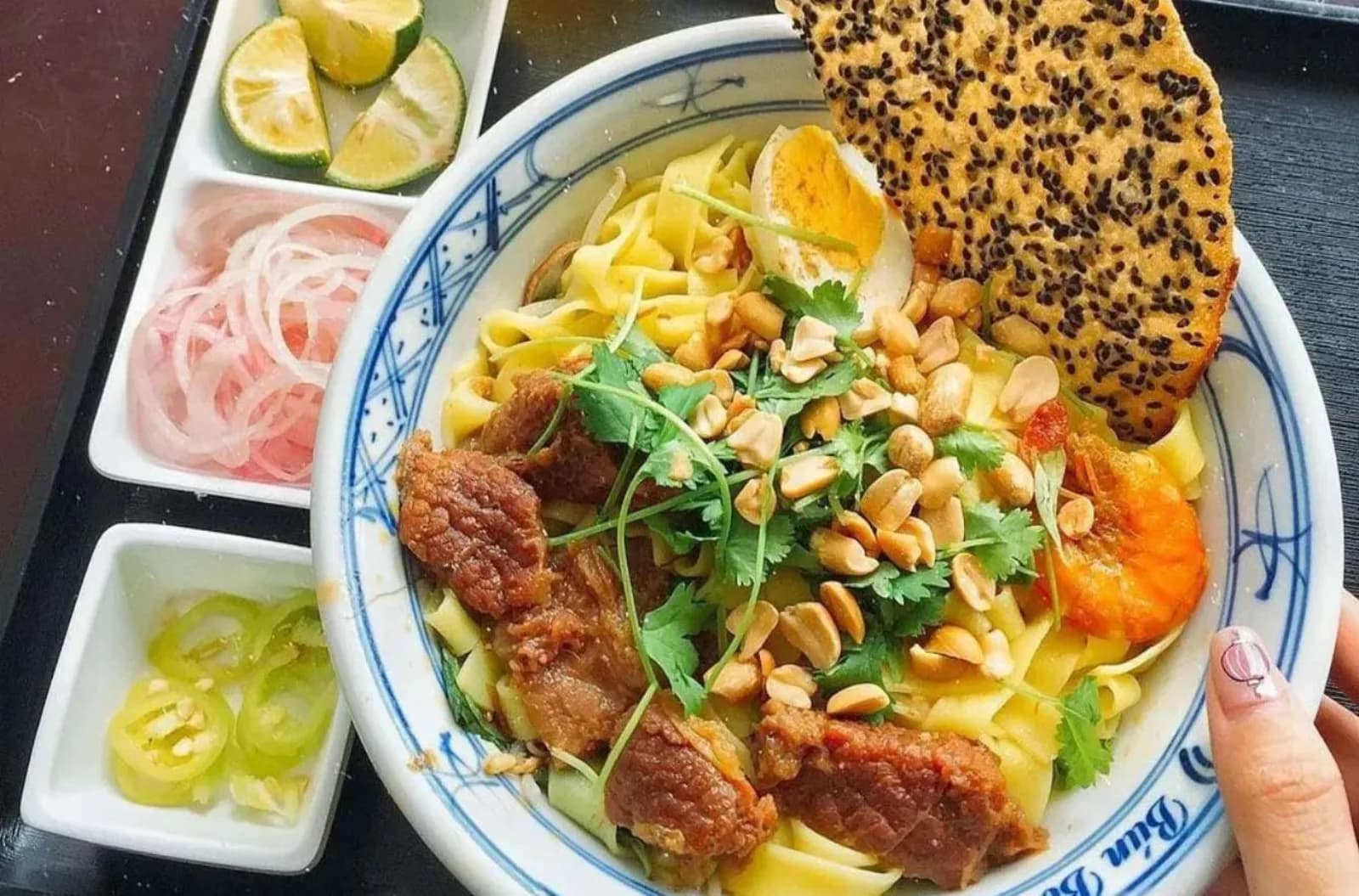 Mi Quang, the turmeric noodle bowl from Quang Nam province, served with rice crackers and peanuts.