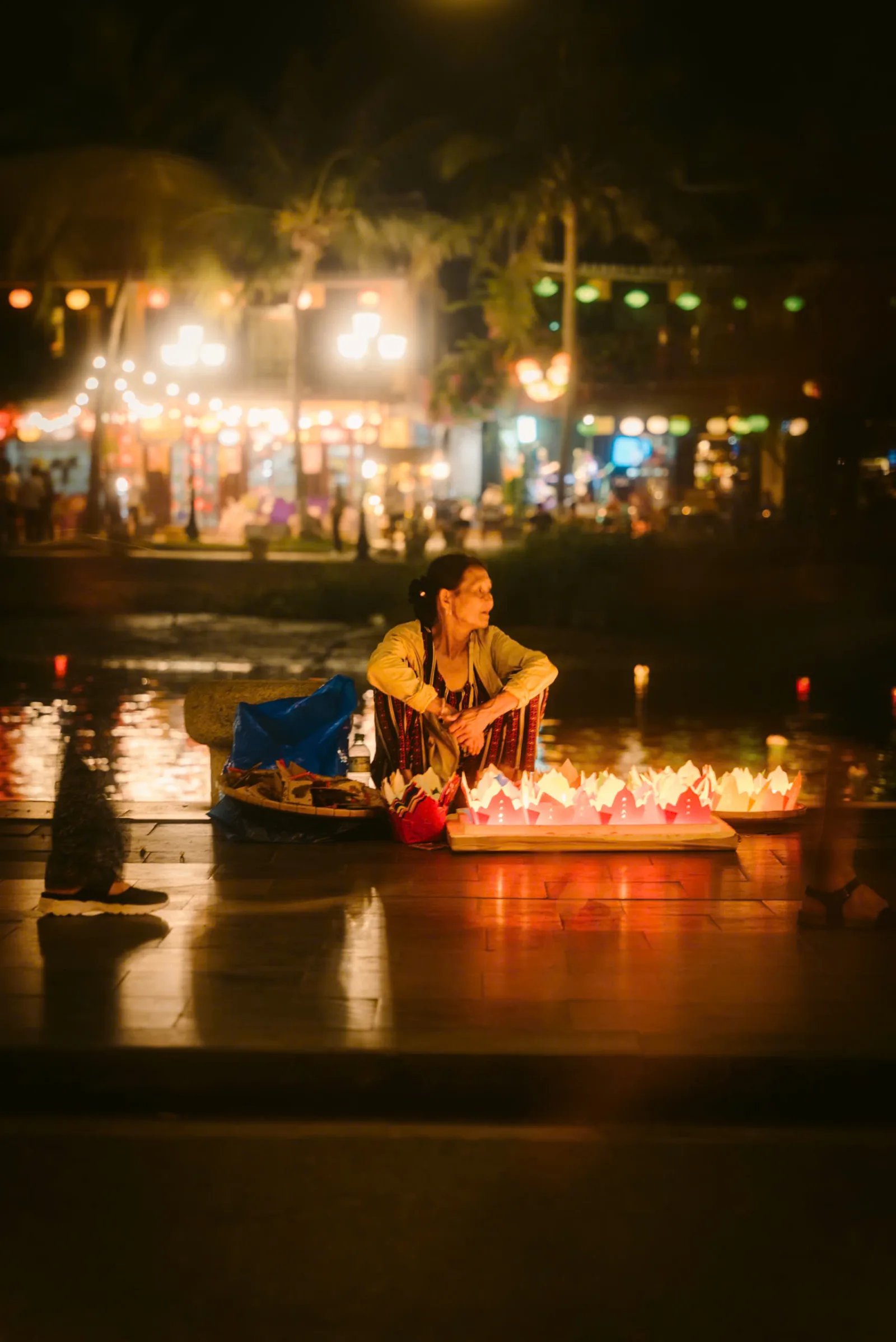 A street vendor selling floating prayer lanterns beside the Hoai River at night.