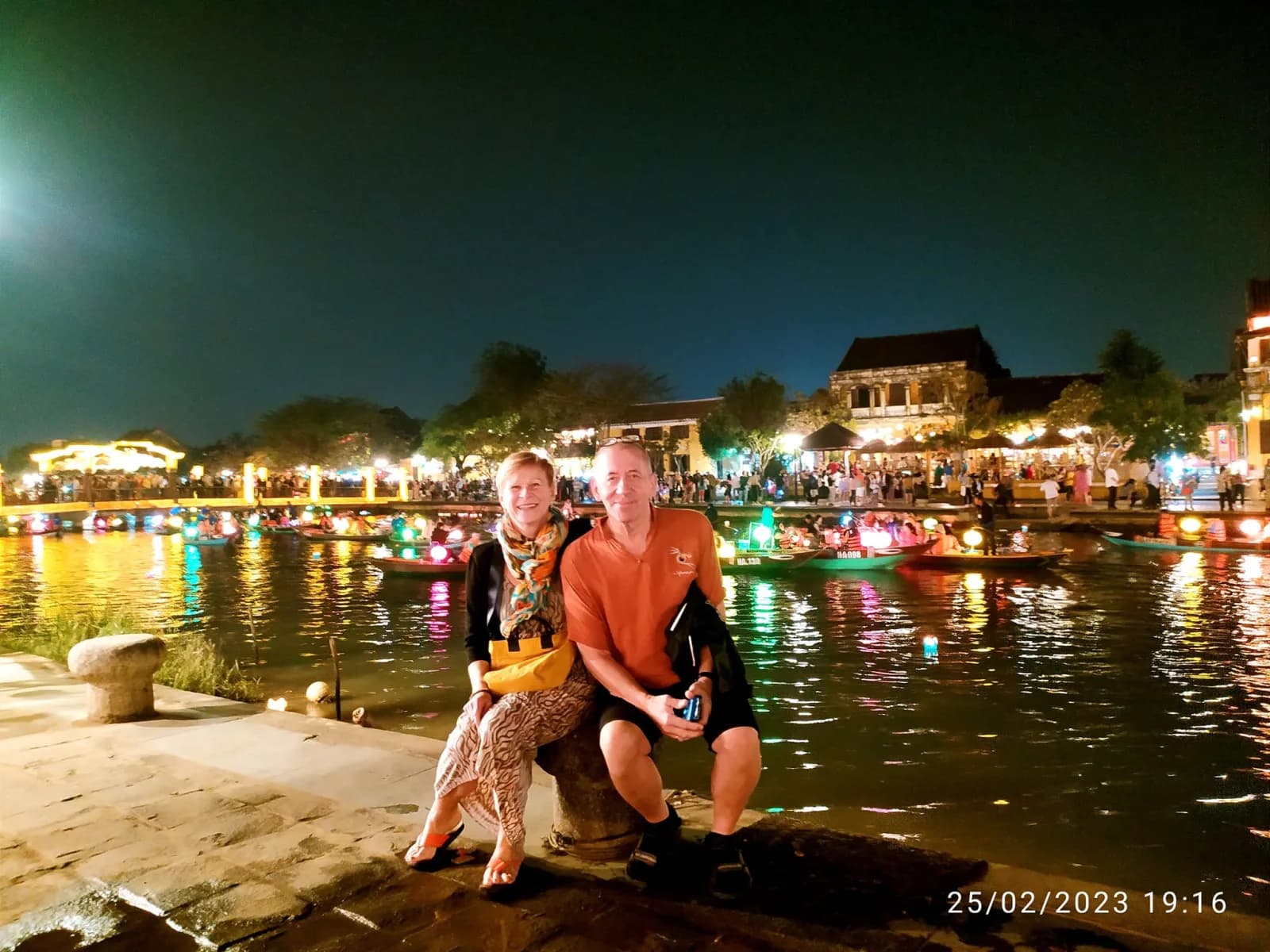 A couple sitting riverside beside floating lanterns glowing on the Hoai River.