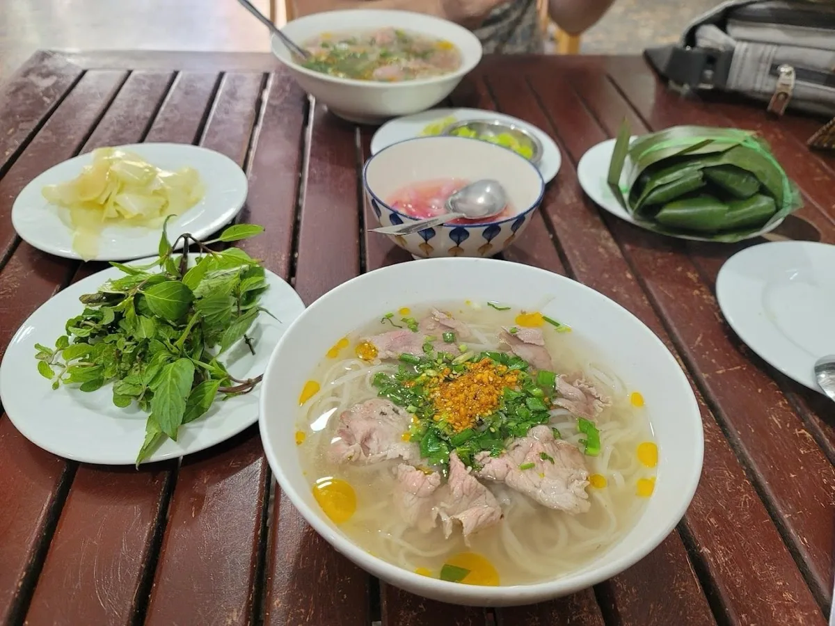 Pho bowl with fresh herbs, pickles and a banana-leaf-wrapped chả roll — the classic Hoi An pairing