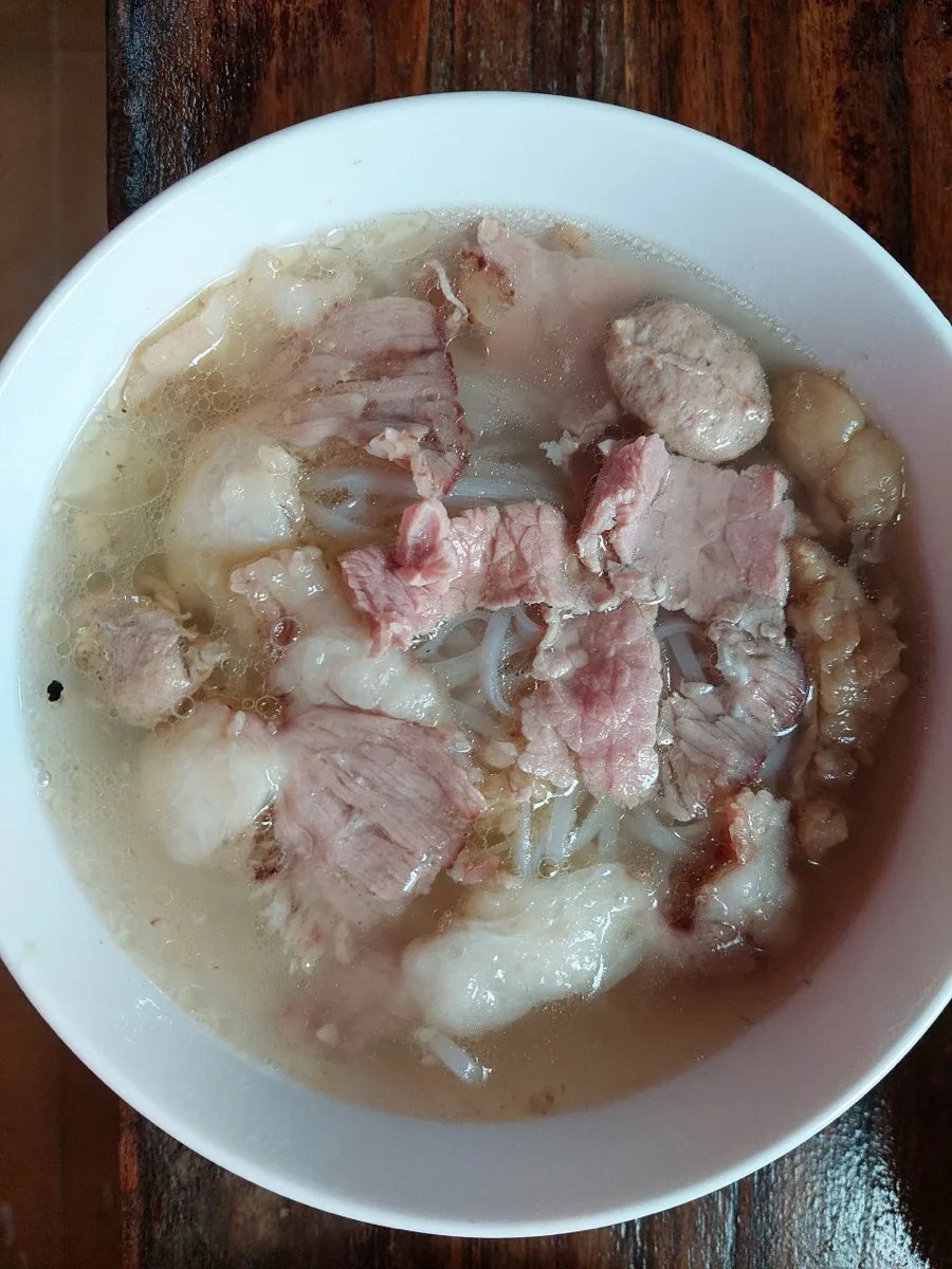 Top-down view of a Hoi An pho bowl with rare beef, brisket and meatballs in clear golden broth