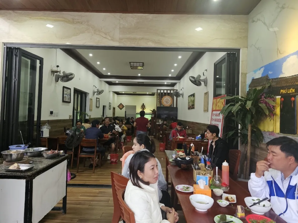 Inside the Phở Liến dining room — long wooden tables, a mural of the old shop, and the prep counter with sliced beef