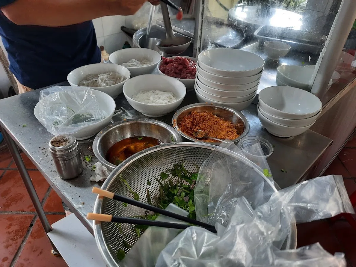 Behind the counter at Phở Mười — the cook blanching sliced beef in the ladle over the simmering stockpot