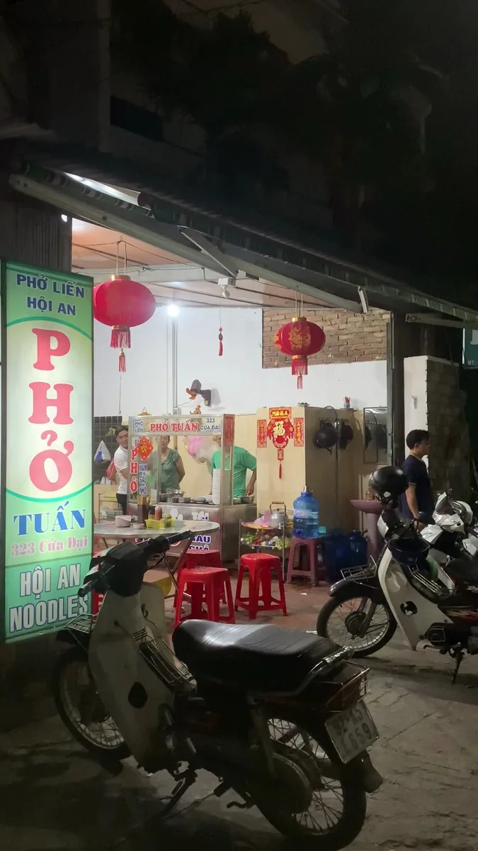 The open noodle cart at Phở Tuấn, 323 Cửa Đại, with the shop sign and red lanterns overhead