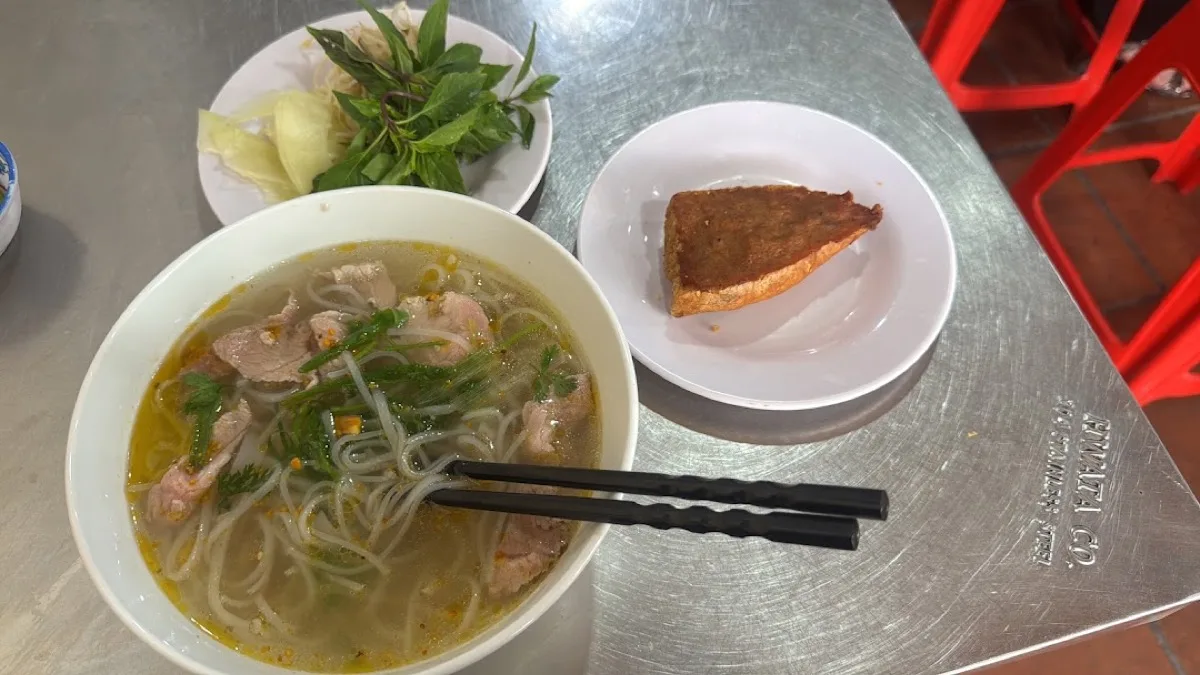 A bowl of pho with herbs and a side of fried bread at Phở Tuấn