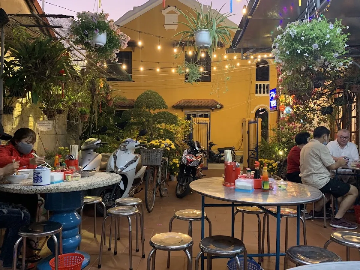 Phở Tùng courtyard at dusk — string lights, potted flowers, and diners at stainless tables