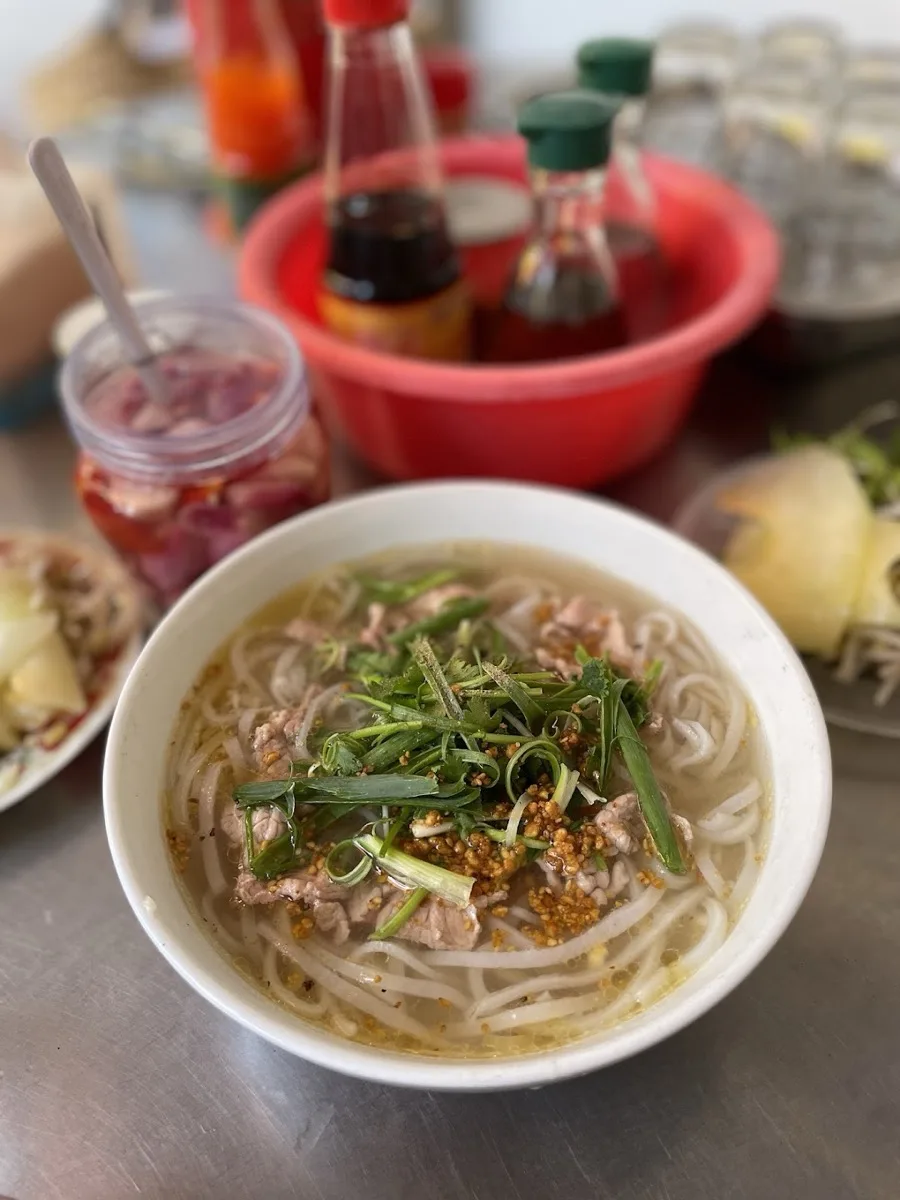 A bowl of pho at Phở Tùng with the condiment tray — pickled onions, chili sauce and the little jars every table keeps