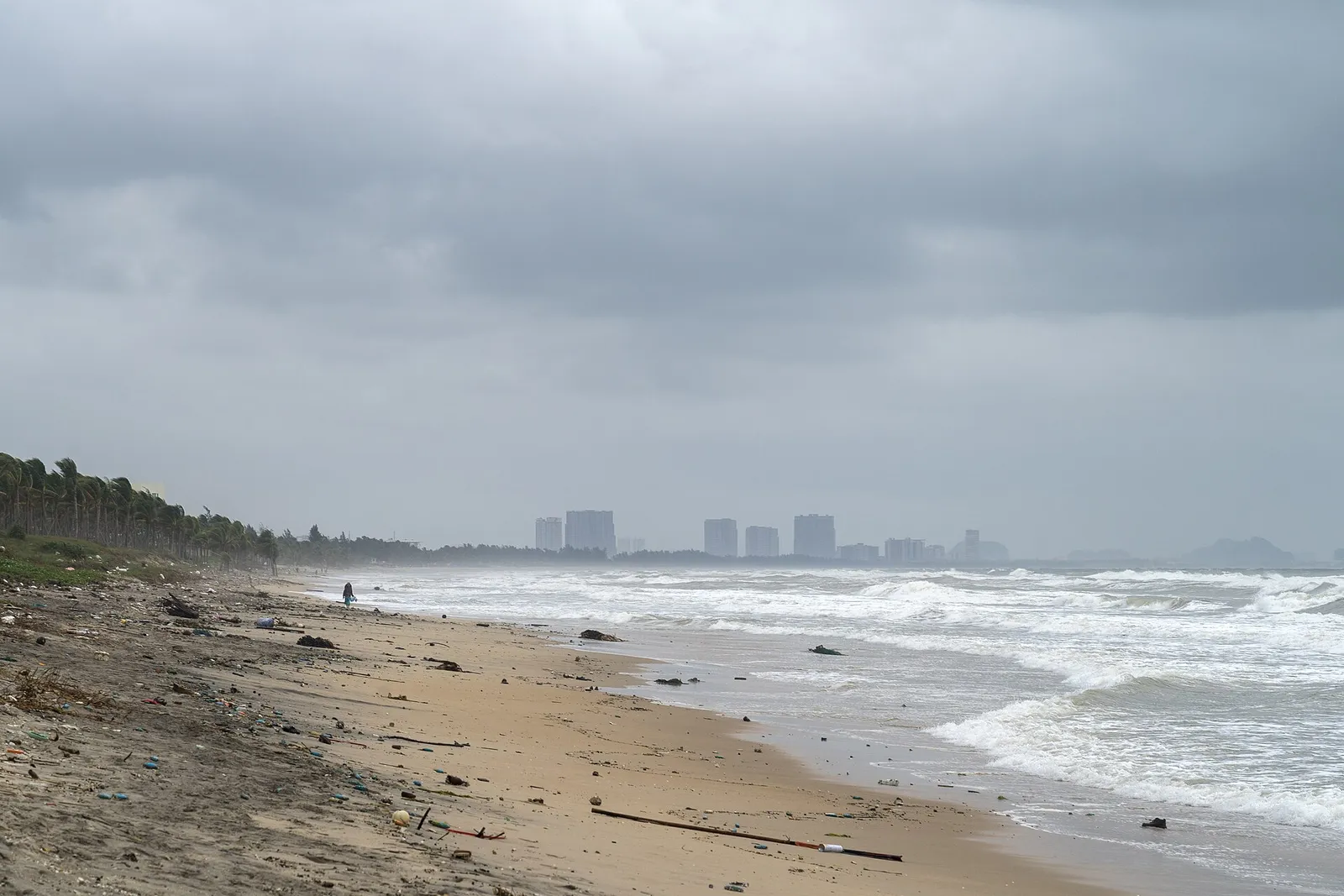 An Bang beach under a grey November sky, rough surf and the Da Nang skyline in the distance.