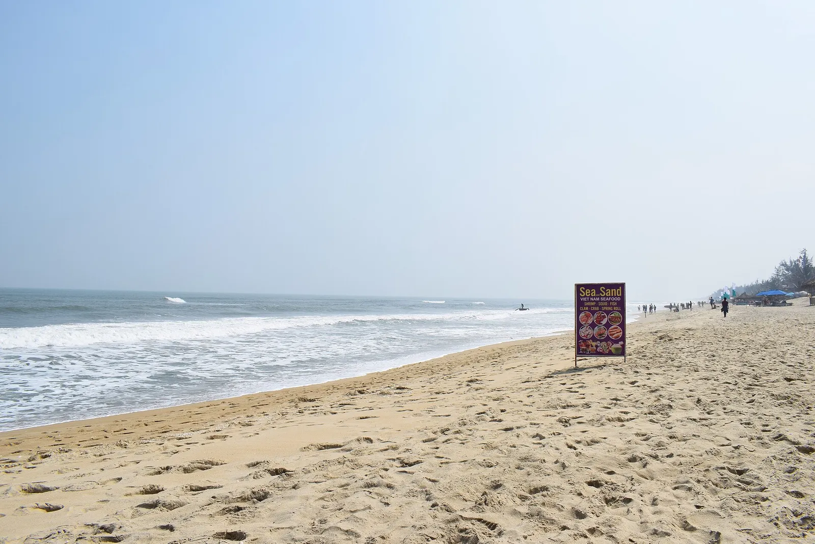The wide sand of An Bang beach near Hoi An, with a few people walking at the water's edge.