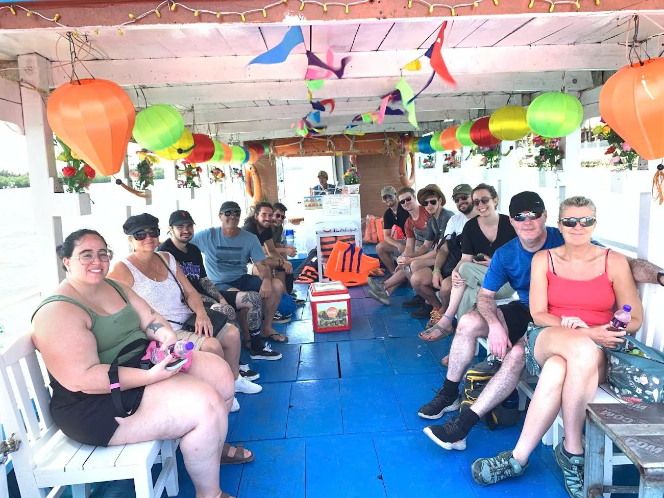 A group seated on a lantern-decorated river boat heading into the Cam Thanh water-coconut palms.