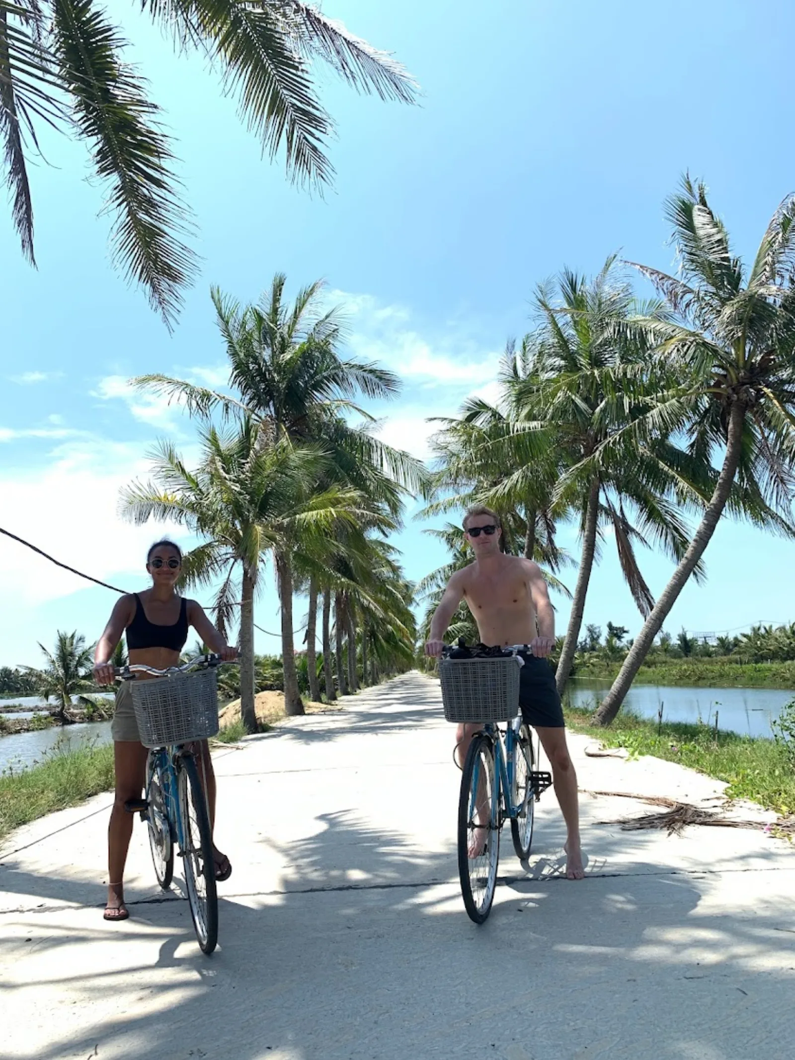 Two guests cycling a shaded countryside lane on the ride out to An Bang beach from Hoi An.