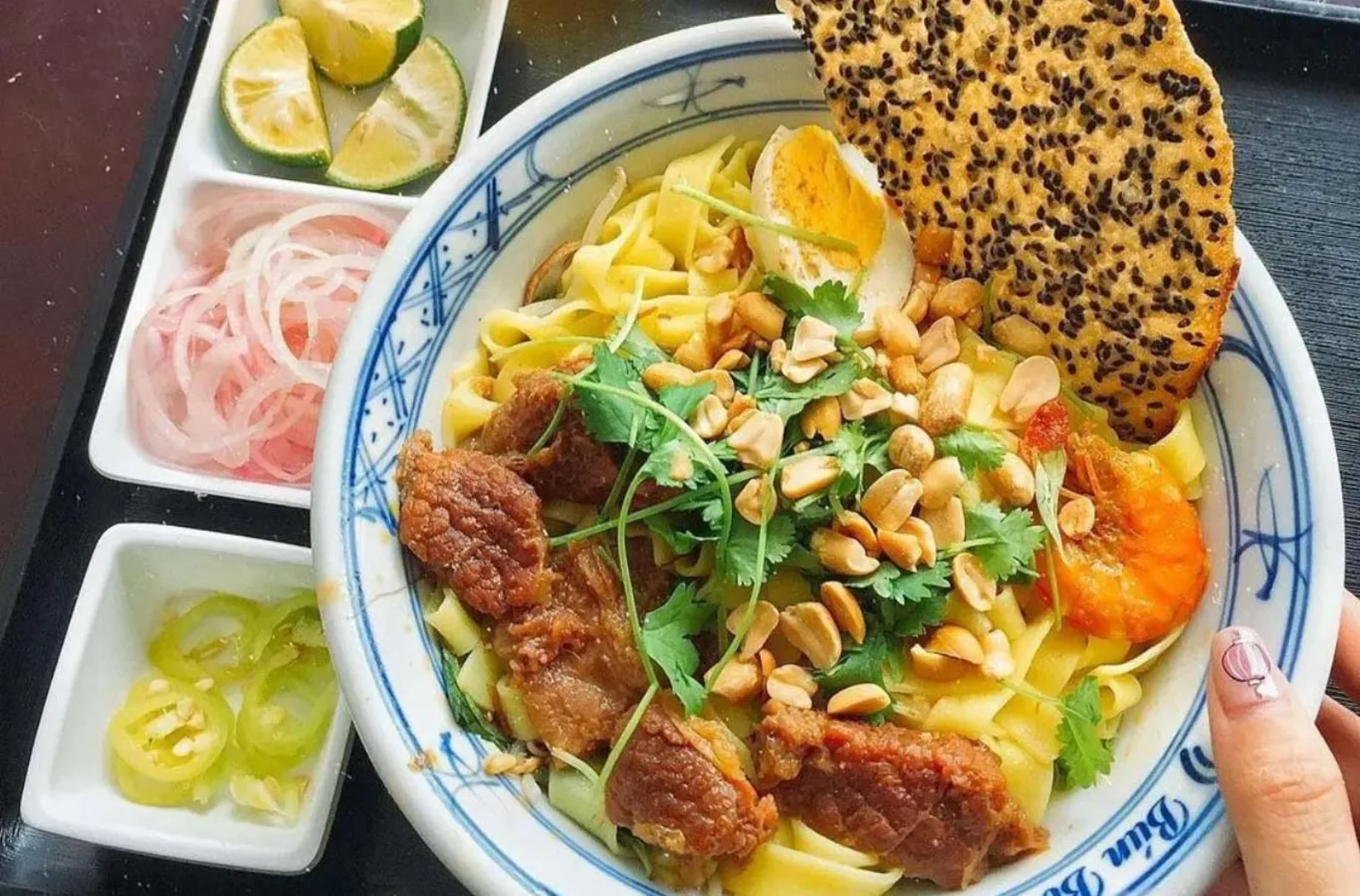A bowl of mi quang with crisp rice cracker, fresh herbs and pickled onion in Hoi An.