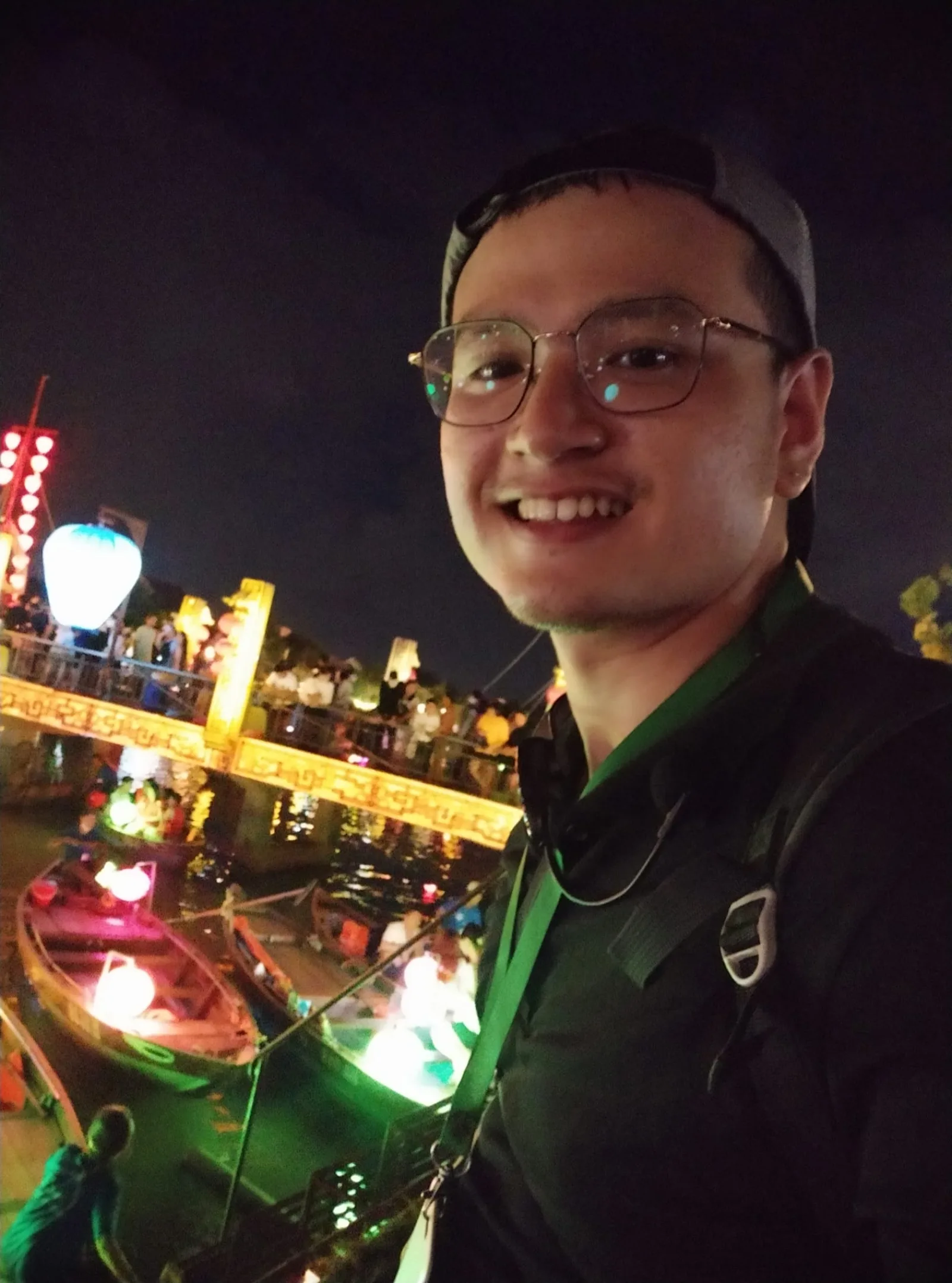 Fin, your private Hoi An tour guide, taking a riverside selfie with lantern-lit boats on the Hoai River at night.