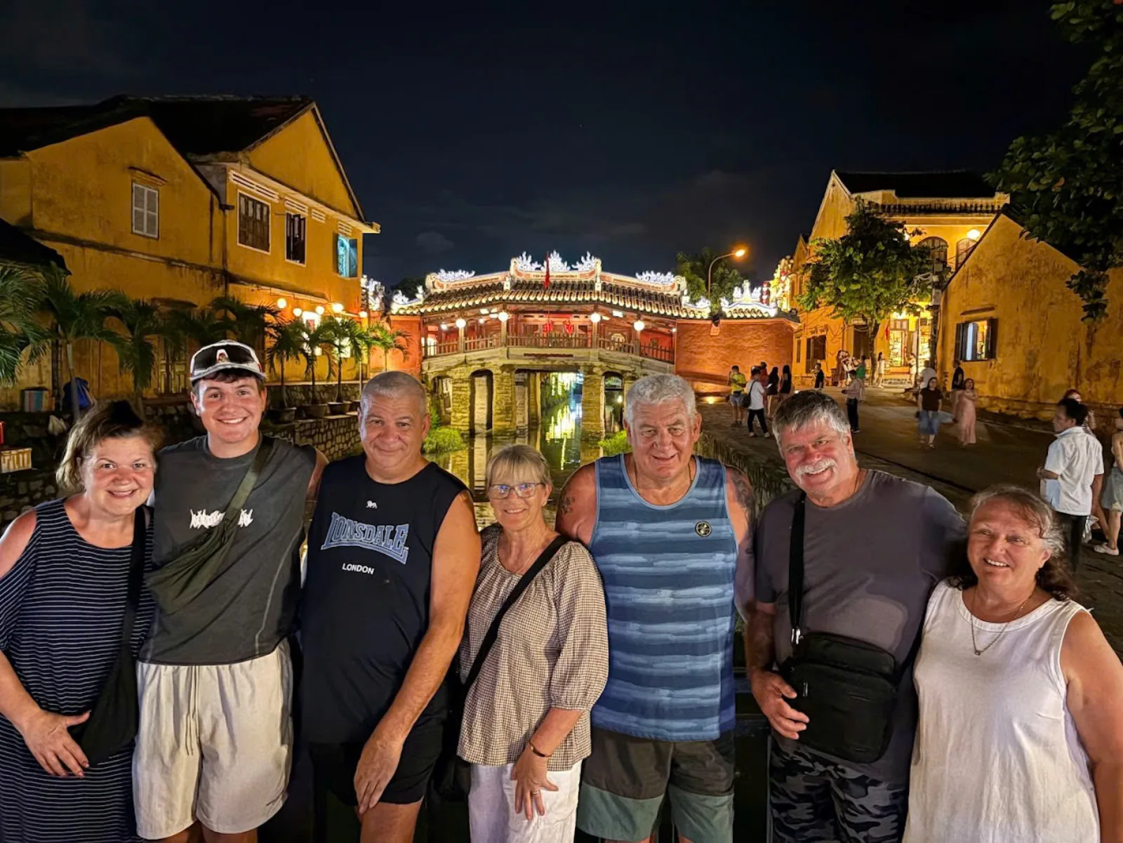 Seven guests with arms around each other in front of the lit Japanese Covered Bridge at night.