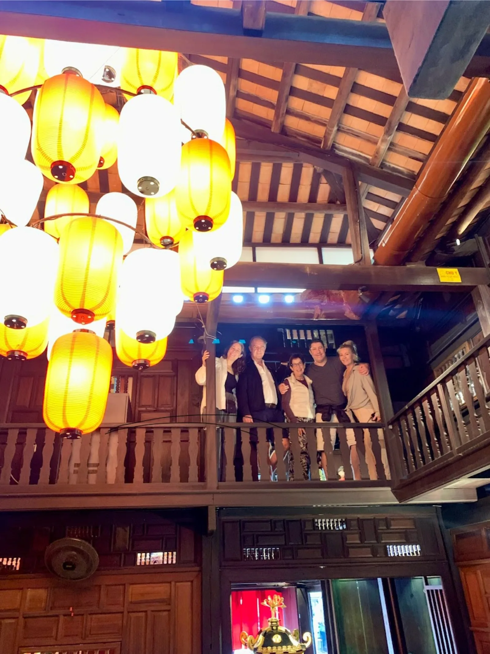 A tour group inside a Hoi An ancient house under a chandelier of silk lanterns.