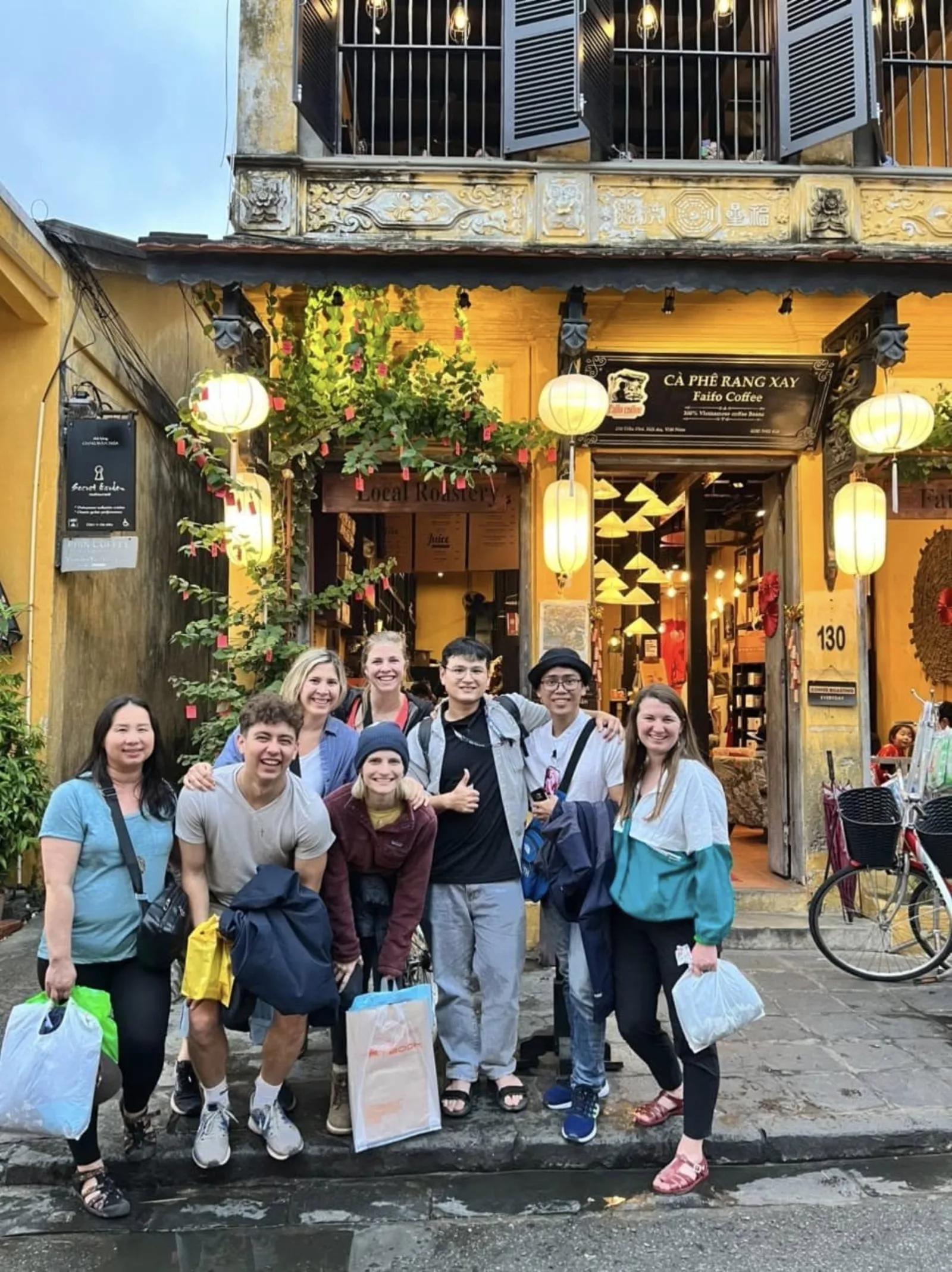 A tour group in front of a yellow-walled cafe in the Hoi An pedestrian area at a quieter hour.