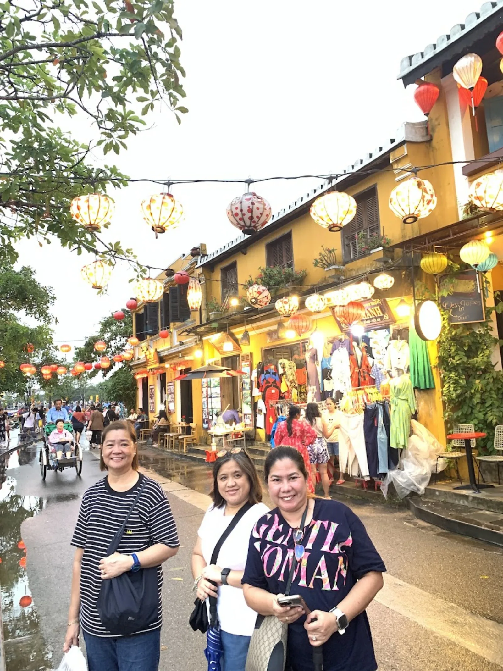 Guests on a lantern-lit Hoi An Old Town street at dusk, shops glowing on both sides.