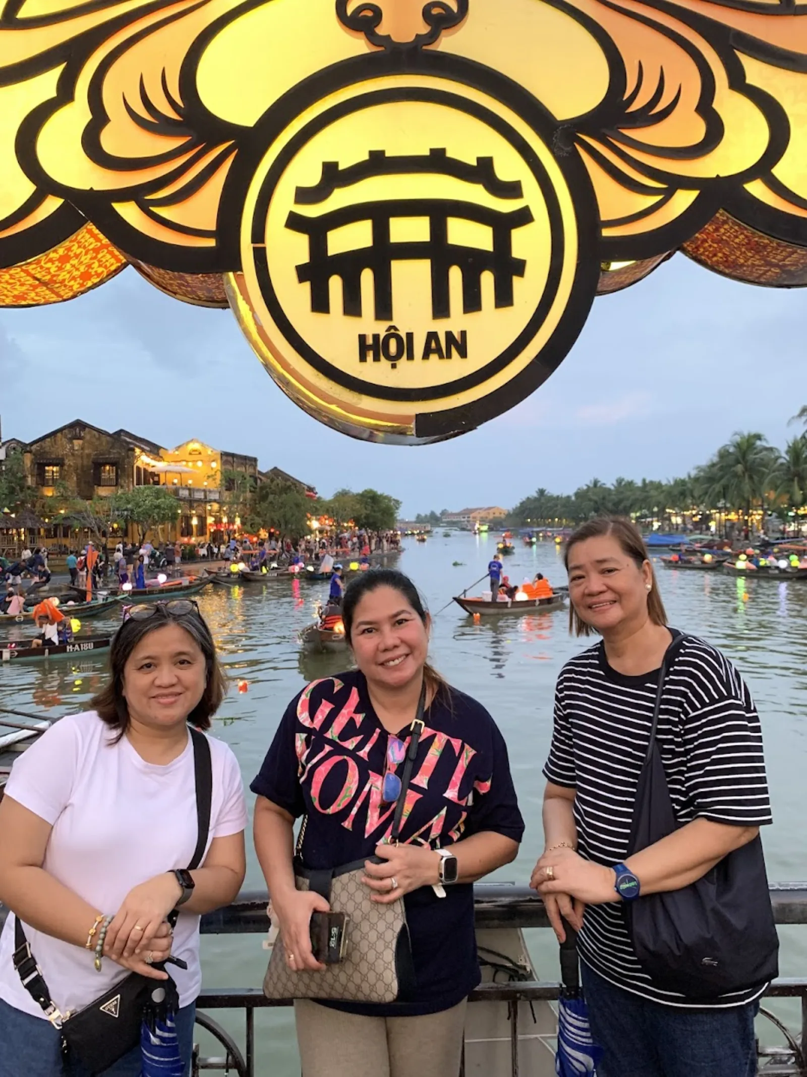 Three travellers by the large HOI AN landmark sign above the Hoai River.