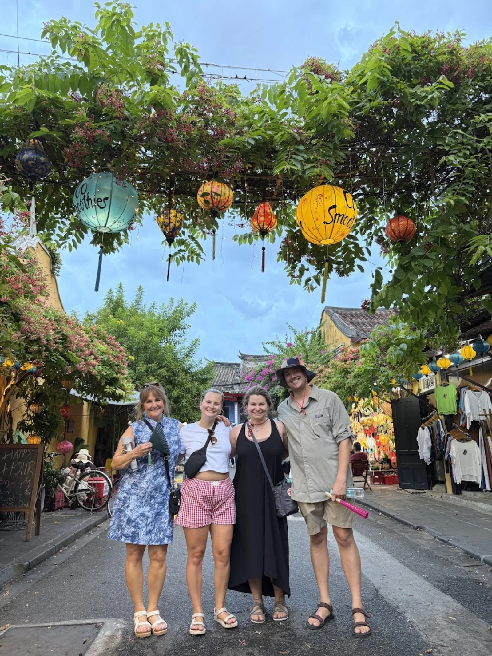 Four guests on a quiet Old Town street shaded by trees and hanging lanterns.