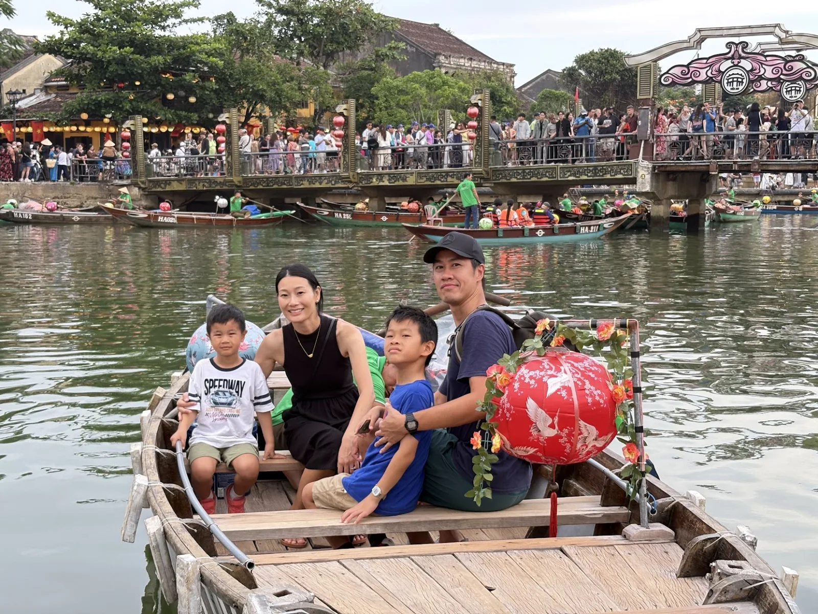 A family of four on a daytime boat ride with the Japanese Covered Bridge behind them.