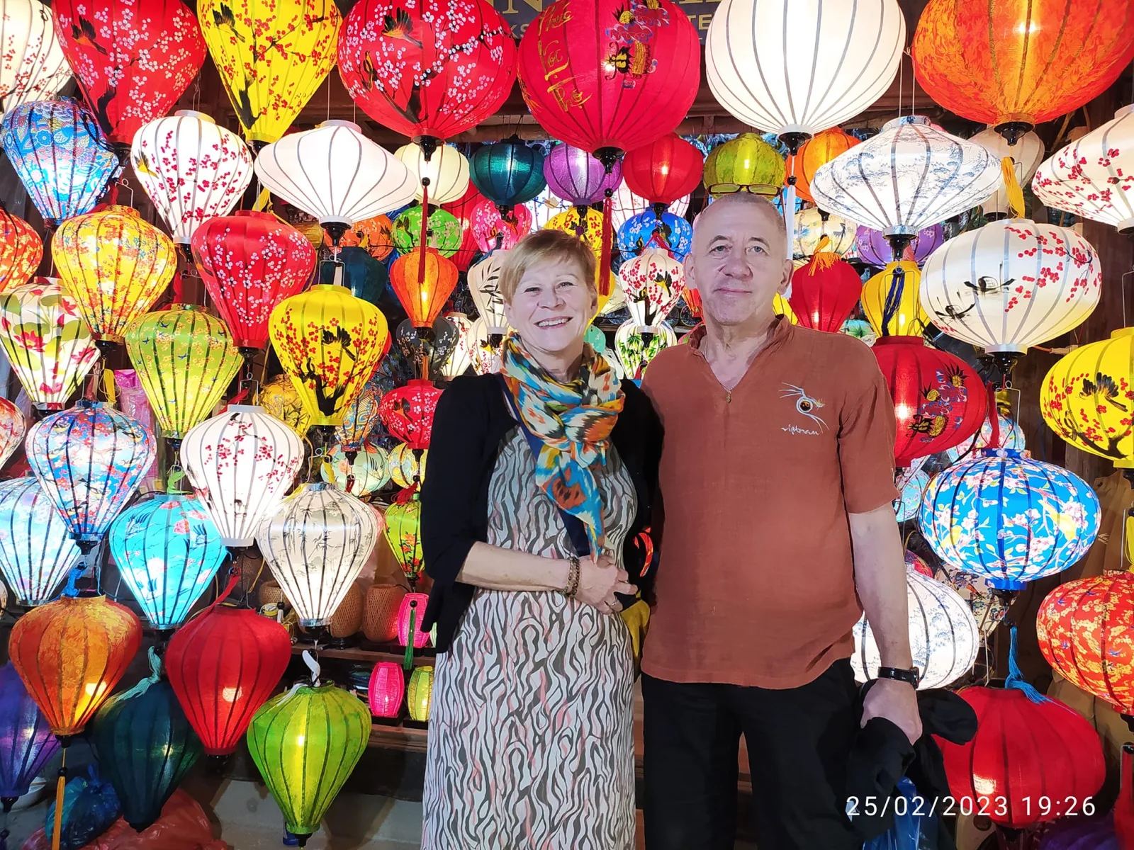 A couple posing before a wall of colourful lanterns on an Old Town street at night.