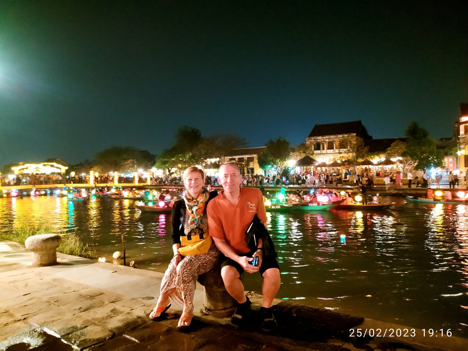 A couple sitting riverside beside floating lanterns glowing on the Hoai River.