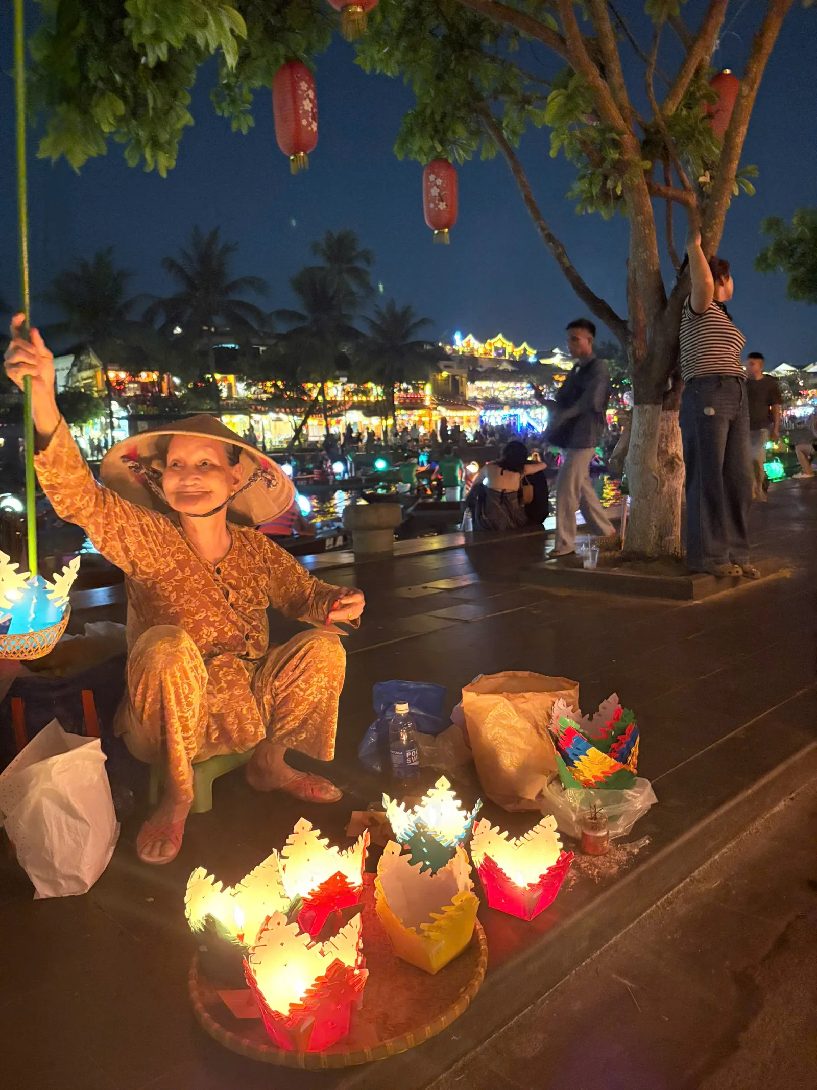 An elderly woman selling handmade lotus lanterns by the Hoai River night market.