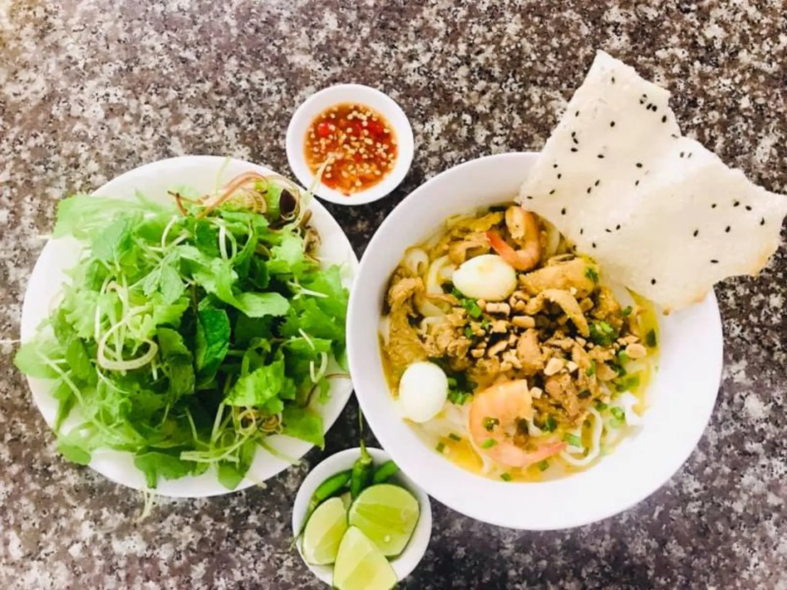 Mi Quang served with sesame rice paper and fresh herbs, the way it is eaten in Quang Nam.